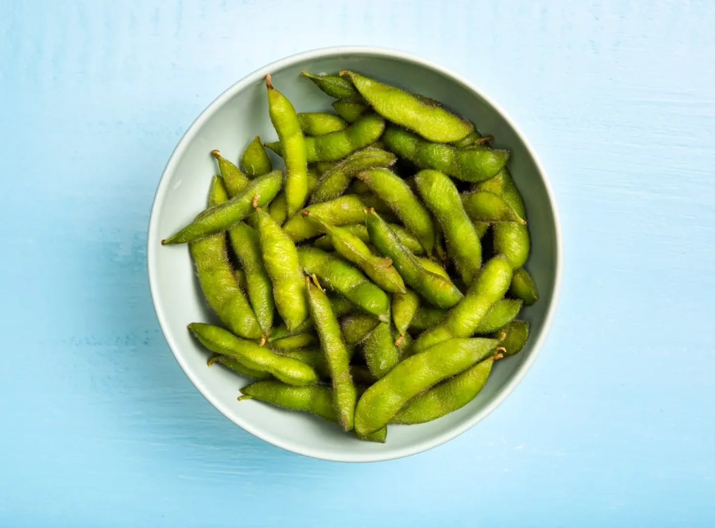 Uma tigela de edamame vista de cima em uma mesa azul.