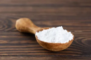 Polvilho: Benefícios e Dicas de Consumo! Colher de pau cheia de polvilho azedo sobre uma superfície de madeira escura. A colher, com cabo longo e rústico, destaca-se contra o fundo uniforme, enquanto o polvilho apresenta uma textura fina e aerada