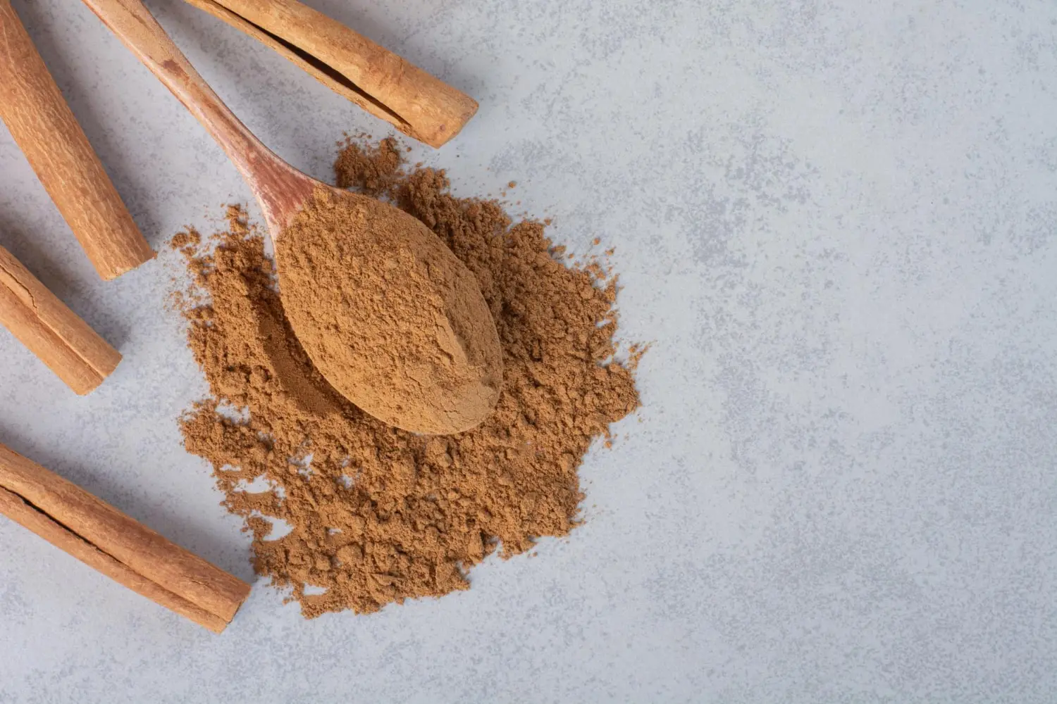 colher de pau com canela em pó, derramando o pó por uma mesa cinza claro