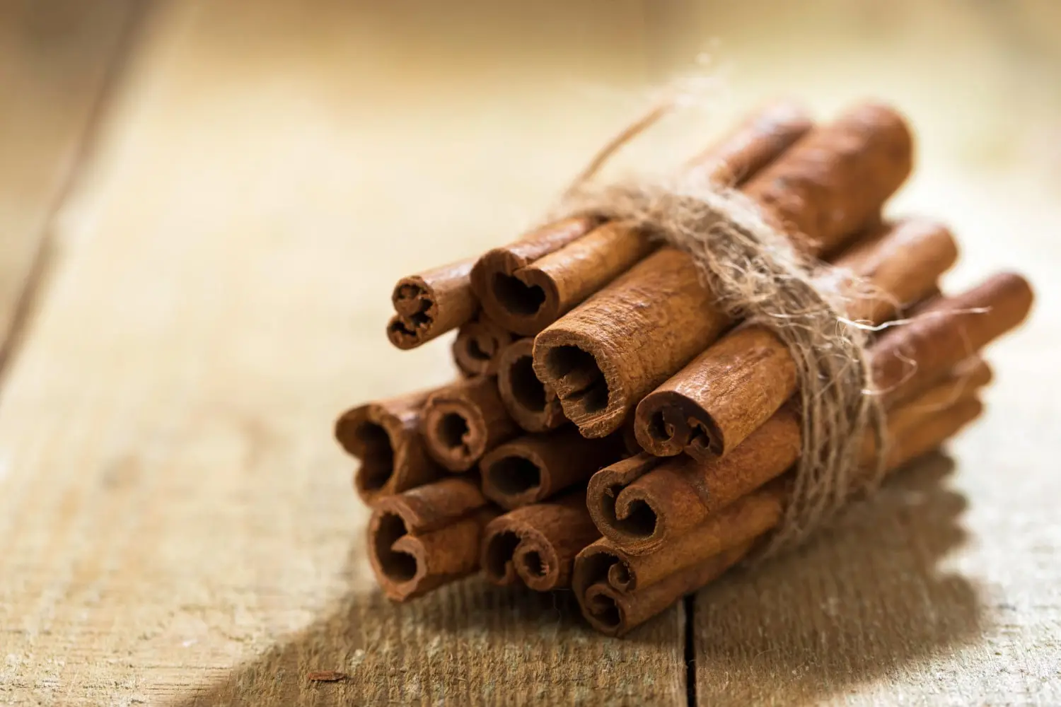 Imagem de um feixe de paus de canela amarrados com um barbante rústico, colocados sobre uma superfície de madeira.