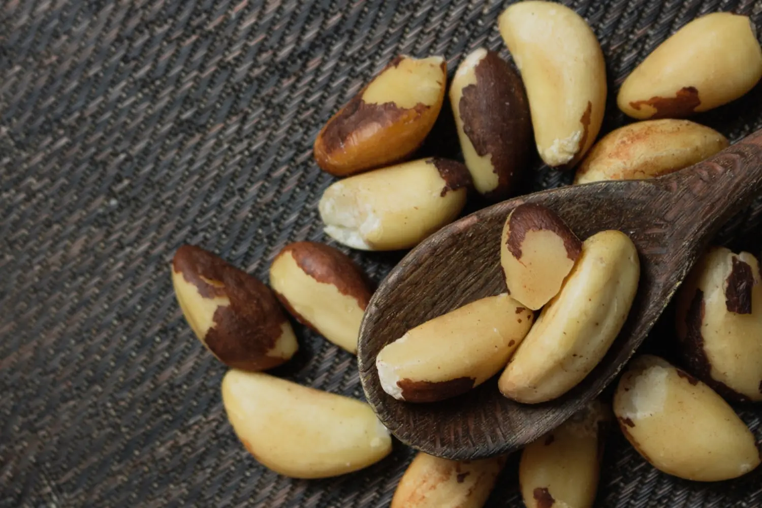 castanhas do para espalhadas por uma mesa cinza escuro e com uma colher de pau com 3 castanhas
