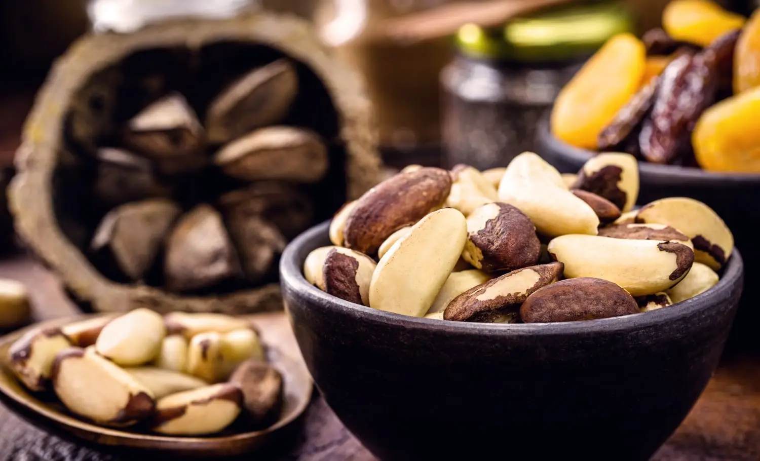 Castanhas-do-pará descascadas em uma tigela escura com cascas de castanha ao fundo em uma mesa rústica.