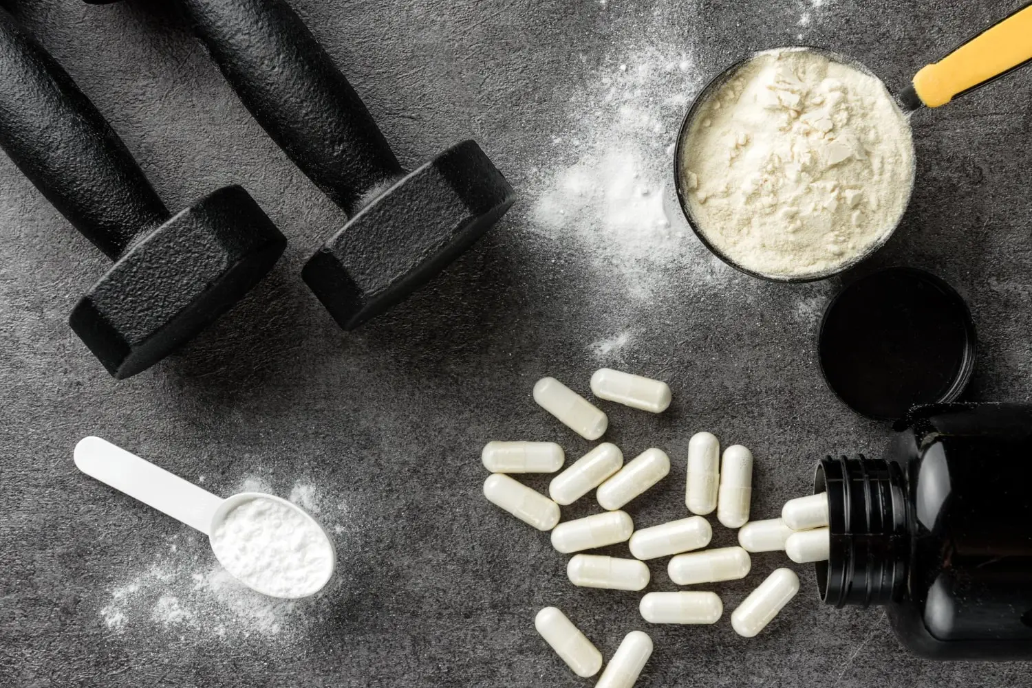 Imagem de suplementos BCAA em cápsulas e pó, dispostos ao lado de halteres de academia, representando o uso de suplementos para melhorar a recuperação muscular e o desempenho em treinos. A imagem mostra uma colher medidora com pó de BCAA, cápsulas e um pote aberto, sugerindo diferentes formas de consumo.