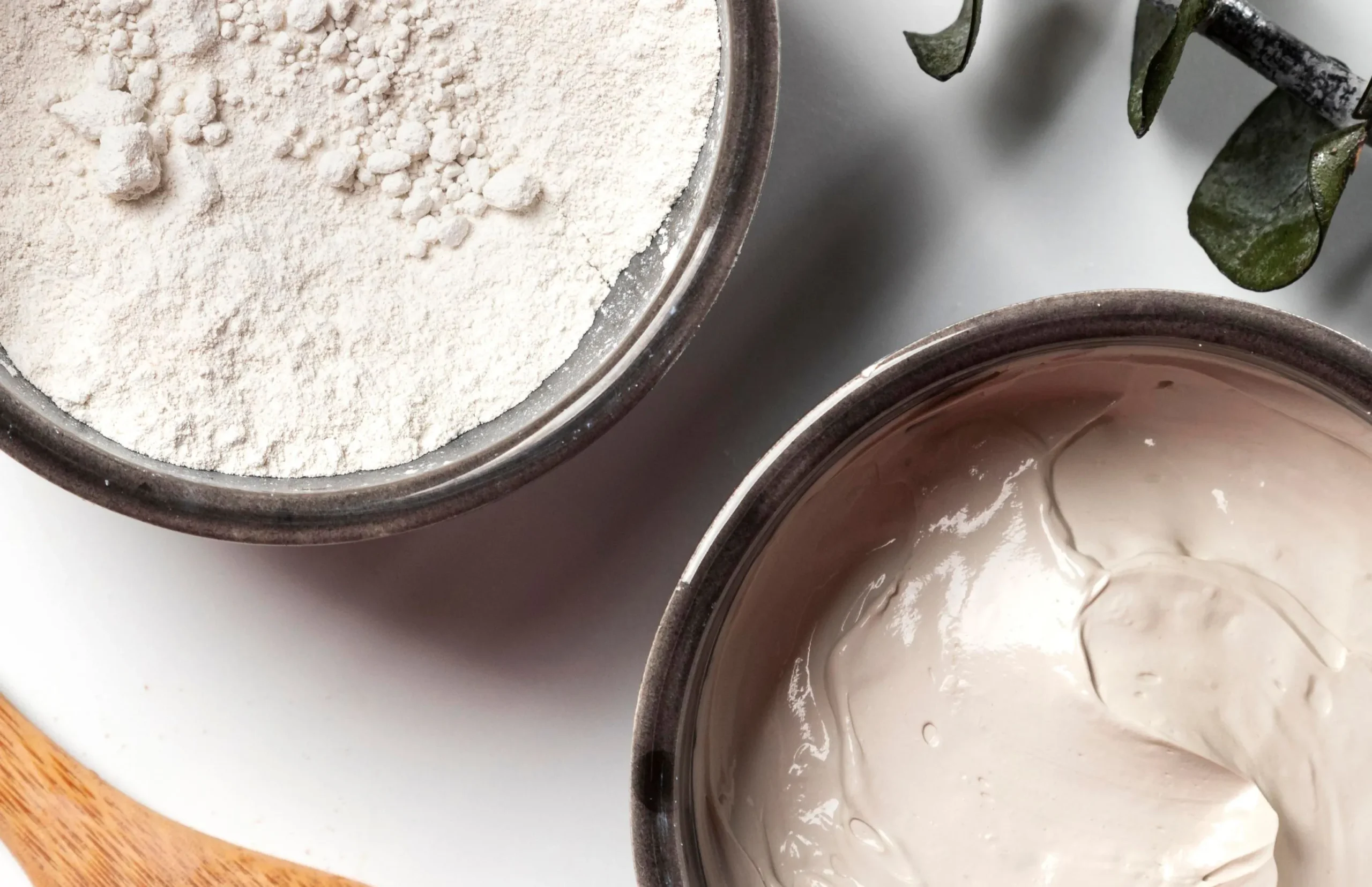 Imagem mostrando dois potes, um contendo goma xantana em pó e outro com uma mistura viscosa de goma xantana. A goma xantana é utilizada como espessante e emulsificante em diversas receitas e produtos.