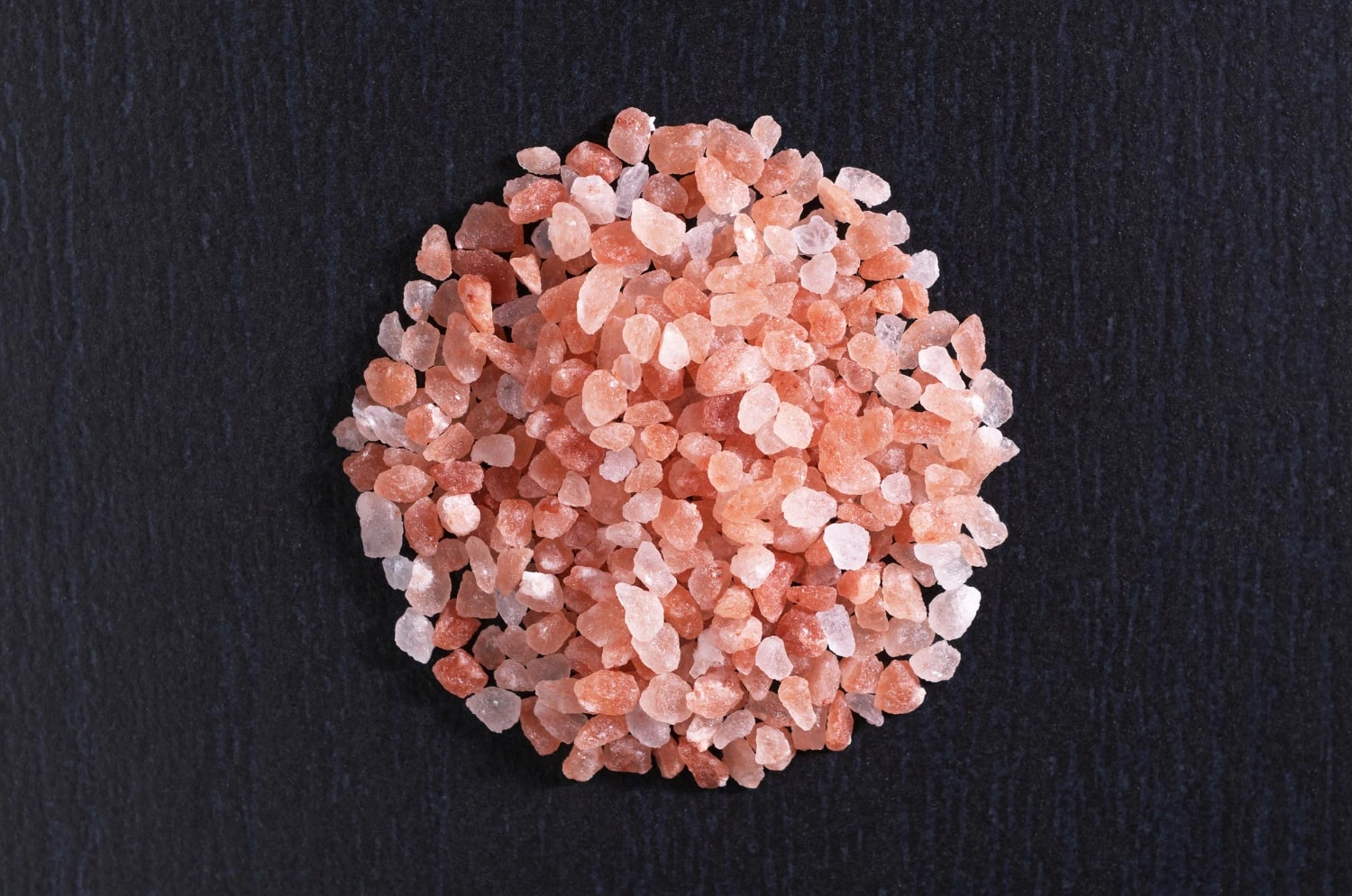Montinho de sal rosa do Himalaia grosso disposto sobre uma superfície preta, destacando a tonalidade rosada dos cristais de sal.