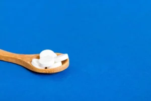 Colher de madeira com comprimidos brancos de magnésio dimalato sobre um fundo azul vibrante.